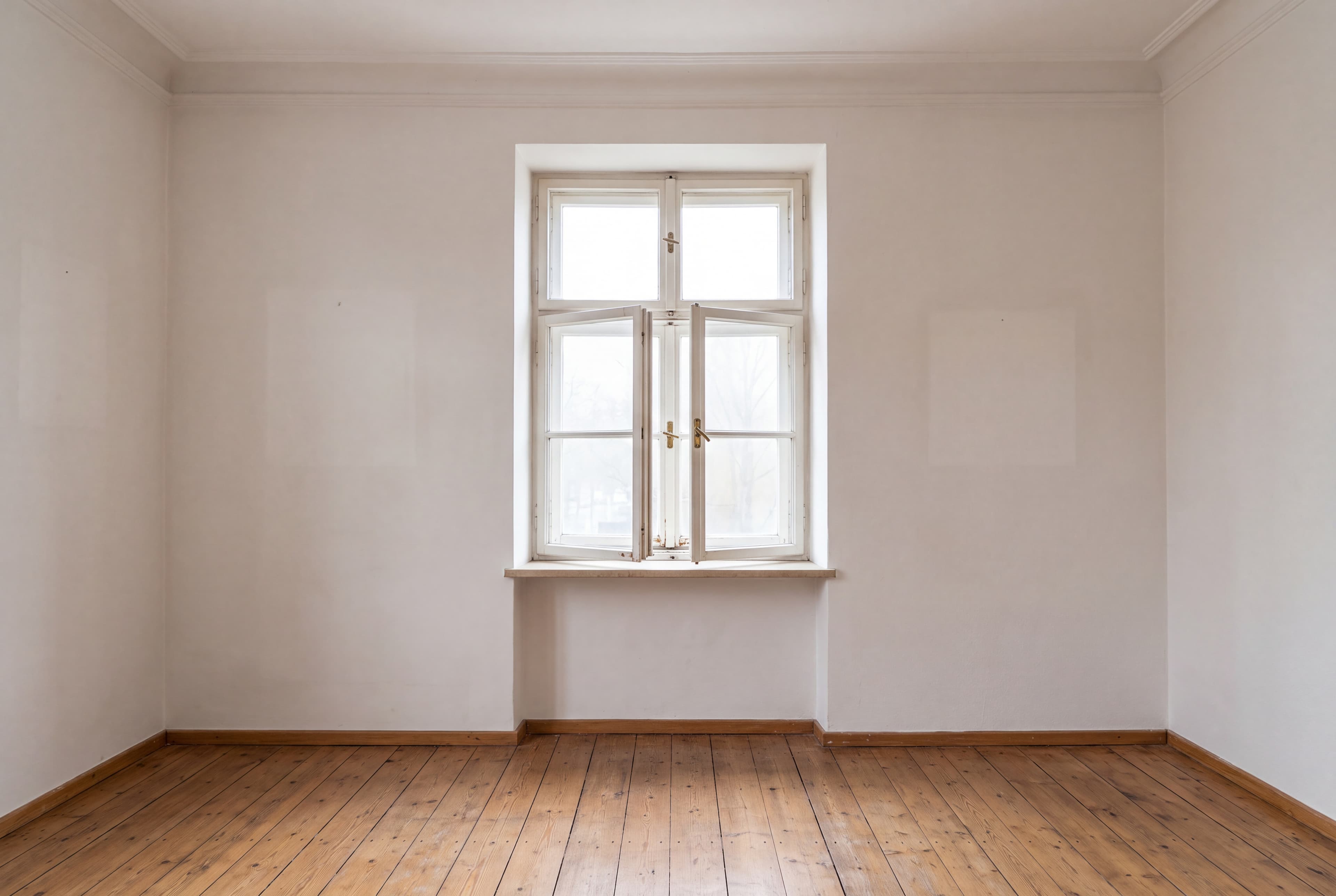 Leerer Raum mit breiten Holzdielen; in der Mitte ein zweiflügeliges Holzfenster, der innere Flügel steht offen. Auf den hellen Wänden zeichnen sich Rechtecke ab, wo Bilder hingen